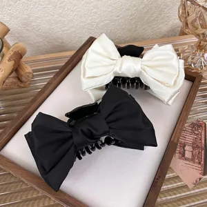 Large satin bow hair claws in black and beige set displayed on a wooden tray