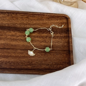 Détail du pendentif feuille de ginkgo doré avec incrustation de nacre et perles vertes