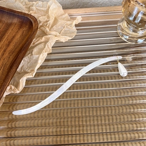 Detail of elegant acetate hair pin with drop pearl charm on a textured tray