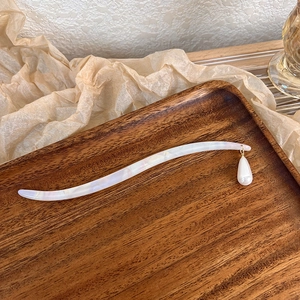 Detailed macro view of S-curve acetate hair pin with drop pearl pendant on wood tray