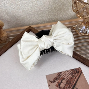 Detail showing creamy satin bow hair claw clip with sturdy black teeth on a wooden surface