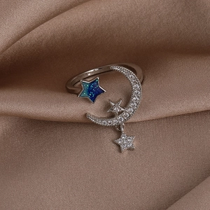 Macro shot of silver moon and star open ring with blue-green zircons on silk fabric