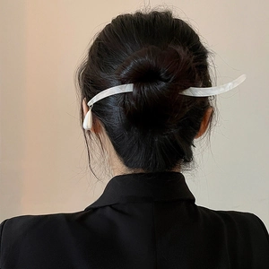 Minimalist white acetate hair stick with pearl drop pendant in a low bun hairstyle
