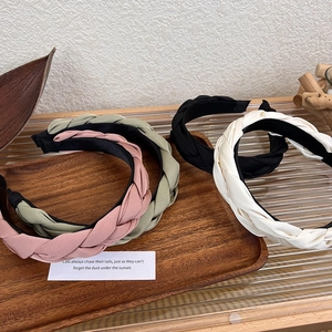 Detail view of four braided satin headbands in pink, green, black and cream on wooden tray