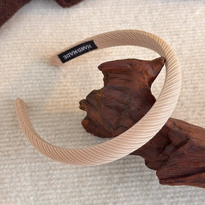 Detail eines beigen Schwamm-Haarreifens mit Twill-Stoffstruktur und Handarbeits-Label