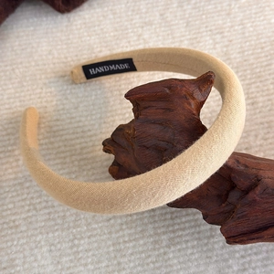 Detail eines beigen Strickstirnbandes mit Handmade-Label auf dekorativem Holz