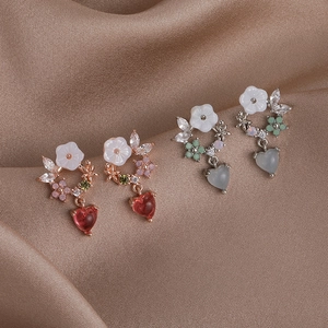 Macro view of colorful zircon flower and heart earrings on elegant brown satin fabric