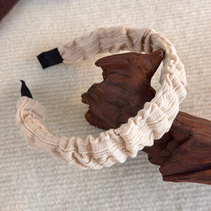 Detail eines cremefarbenen gefalteten Schwamm-Haarreifs mit strukturierter Strickware