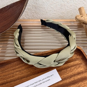Detail of olive green satin braided headband with non-slip lining on a wooden tray
