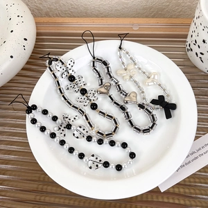 Detail of five black and white beaded phone charms with bows and hearts in a ceramic bowl