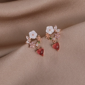 Detail macro shot of floral zircon earrings with heart pendant on satin fabric