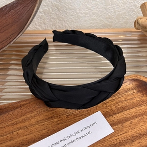 Close-up of black braided satin headband with textured finish on a wooden tray