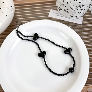 Detailed view of a black beaded phone strap with glossy heart charms on a white plate