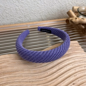 Dettaglio di una fascia lavorata a maglia viola con trama a spina di pesce ed etichetta