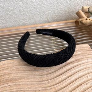 Dettaglio della trama tessuta a mano e dell'etichetta di una fascia in maglia nera
