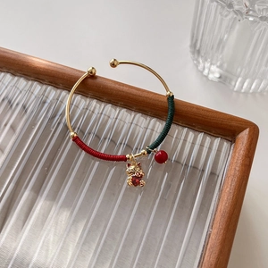 Detail of gold open bangle with red and green cord wrapping and lucky cat charm