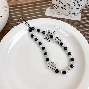 Detailed shot of black and white beaded phone strap with heart and cross charms in a tray
