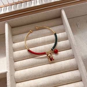 Macro detail of gold bangle with red and green cord wrap and lucky cat charm