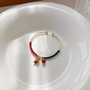 Golden cat pendant bracelet with red woven rope and zircon accents on a white plate