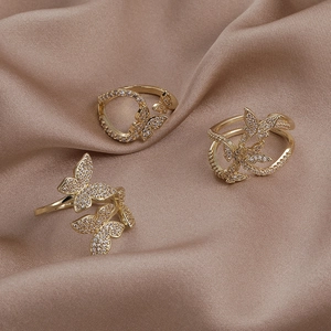 Detailed view of three gold butterfly rings with cubic zirconia on silk fabric