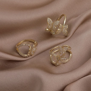 Detailed view of three gold butterfly rings with cubic zirconia on silk fabric