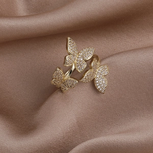 Detailed macro view of triple zircon butterfly rings resting on elegant brown silk fabric