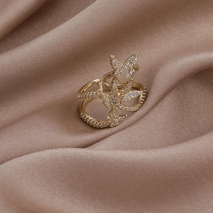 Macro detail of golden open ring featuring three zircon butterflies on champagne silk fabric