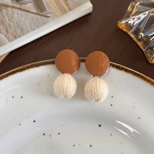 Détail de boucles d'oreilles vintage avec laque marron et boule de laine blanc crème