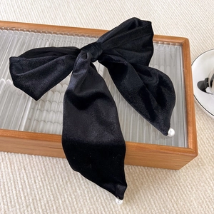Detail of elegant black velvet bow hair clip with decorative pearls on wooden tray