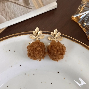 Gros plan de boucles d'oreilles boules en peluche marron avec feuilles dorées et perles