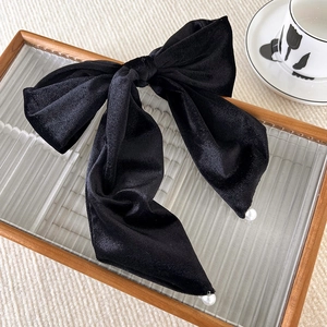 Detail of elegant black velvet hair bow clip with white pearl accents on wooden tray