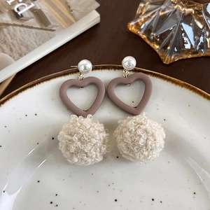 Détail de boucles d'oreilles d'hiver avec cœurs bruns et pompons en laine d'agneau