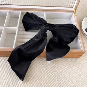 Detailed close-up of large black velvet bow hair clip with elegant pearl accents on ribbons
