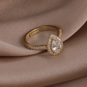 Detailed macro view of gold halo ring with pear-cut zircon on champagne silk fabric