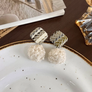 Détail de boucles d'oreilles d'hiver avec carrés en tweed et boules de peluche blanches
