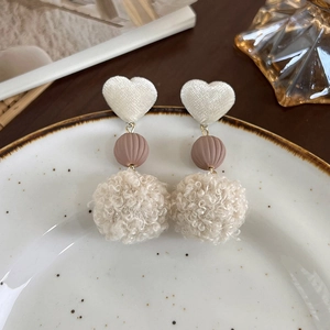 Gros plan sur des boucles d'oreilles d'hiver avec cœurs en velours et pompons en peluche