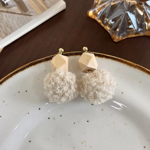 Détail de boucles d'oreilles boules en laine d'agneau et perles géométriques en bois