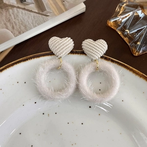 Détail de boucles d'oreilles d'hiver avec cœur en velours et pompon en peluche grise