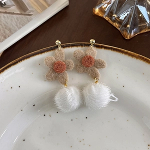 Détail de boucles d'oreilles fleur en peluche avec pompon en fausse fourrure blanche