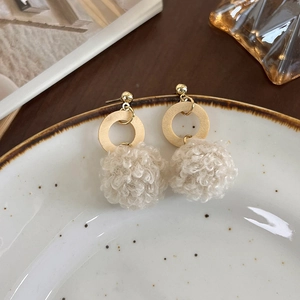 Détail de boucles d'oreilles automne avec pompons crème et anneaux en bois sur plateau