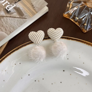 Détail de boucles d'oreilles cœur en peluche avec pompon beige doux sur plat céramique