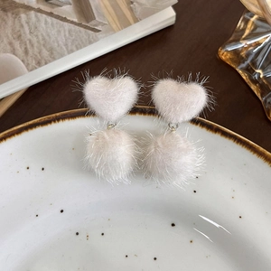 Détail de boucles d'oreilles en fausse fourrure rose poudré avec cœurs et pompons