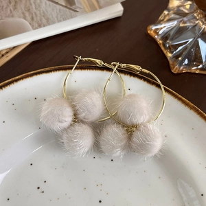 Détail de boucles d'oreilles créoles dorées avec pompons en peluche beige sur plat vintage