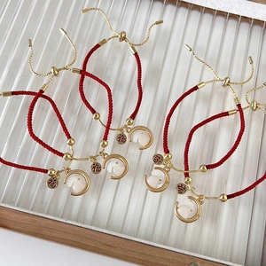 Detail van de rode touwarmband met gouden Fu-plaatje en maankonijn-bedeltje in close-up
