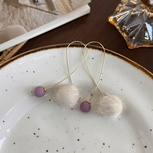 Vue détaillée du pompon blanc doux et de la perle violette sur les boucles dorées
