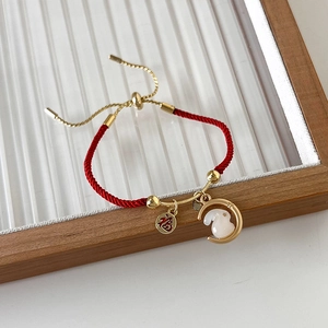 Detail van rode gevlochten armband met gouden Fu-bedel en wit konijnenhangertje