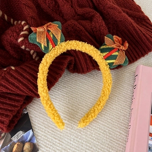 Detail of yellow plush Christmas headband featuring festive green gift box decorations