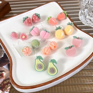 Detailed view of assorted flocked fruit stud earrings displayed on a white ceramic plate