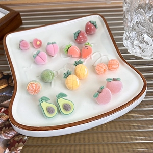 Detailed close-up of colorful flocked fruit stud earrings set on a toast-shaped ceramic tray