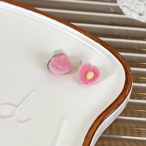Detail of flocked peach earrings with realistic texture and leaf accents on a ceramic plate